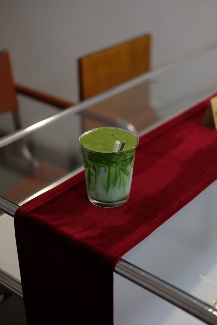 Glass of green matcha latte on a table with a red runner, modern indoor cafe setting.