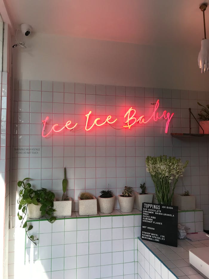 A stylish ice cream shop featuring a vibrant neon sign and potted plants.